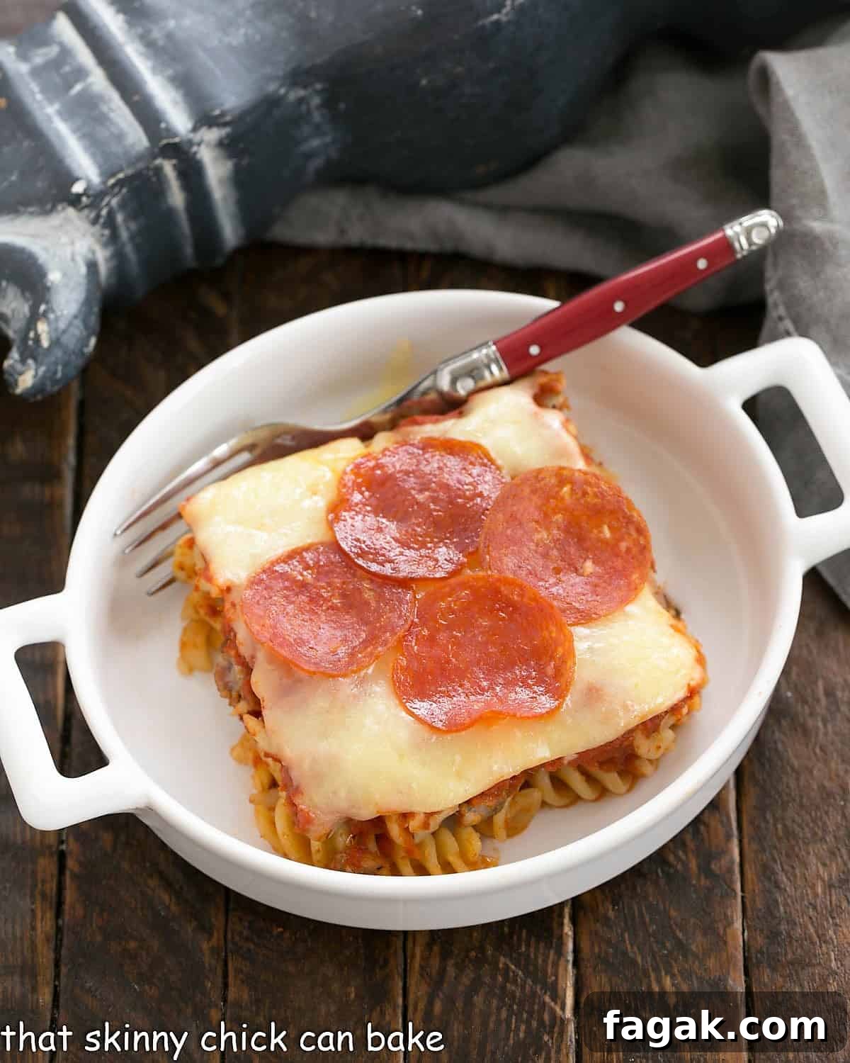 Overhead view of one sliced of pizza casserole in a white dish with a red handle fork.