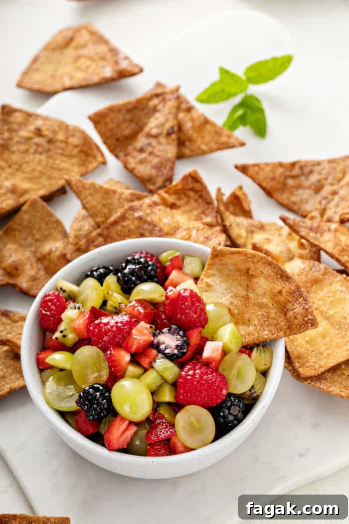 Cinnamon chip in a bowl of fruit salsa, with more cinnamon chips in the background.