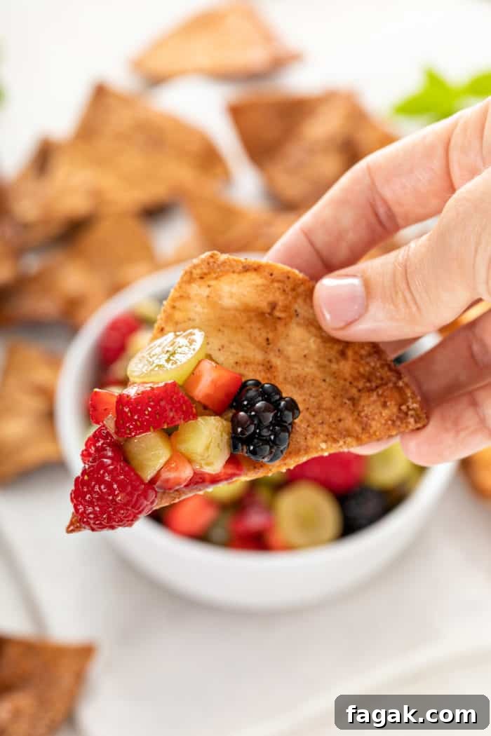 Hand holding up a cinnamon chip with a scoop of fruit salsa on it.