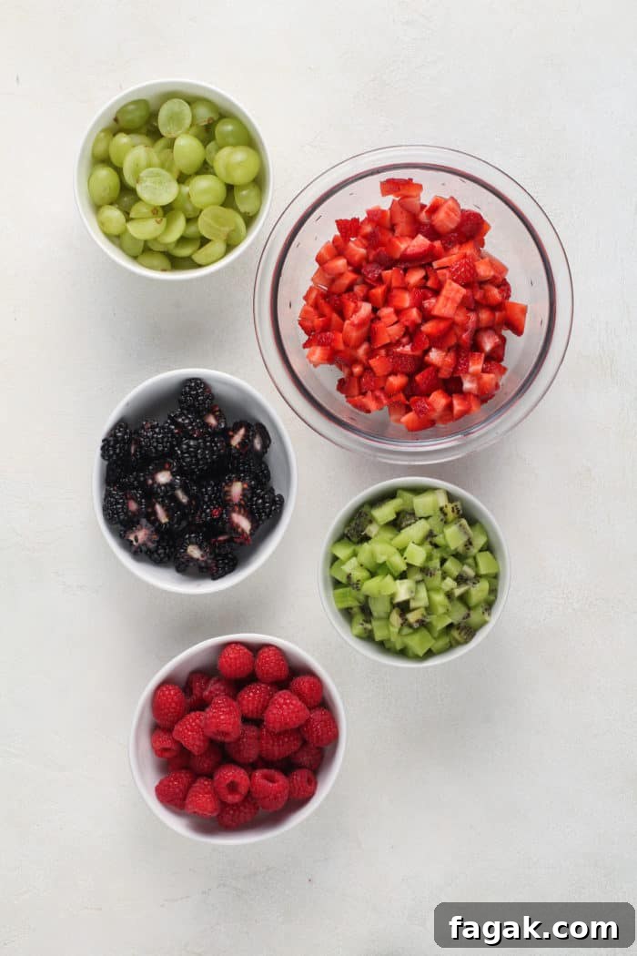 Bowls of diced fresh fruit for fruit salsa arranged on a white countertop.