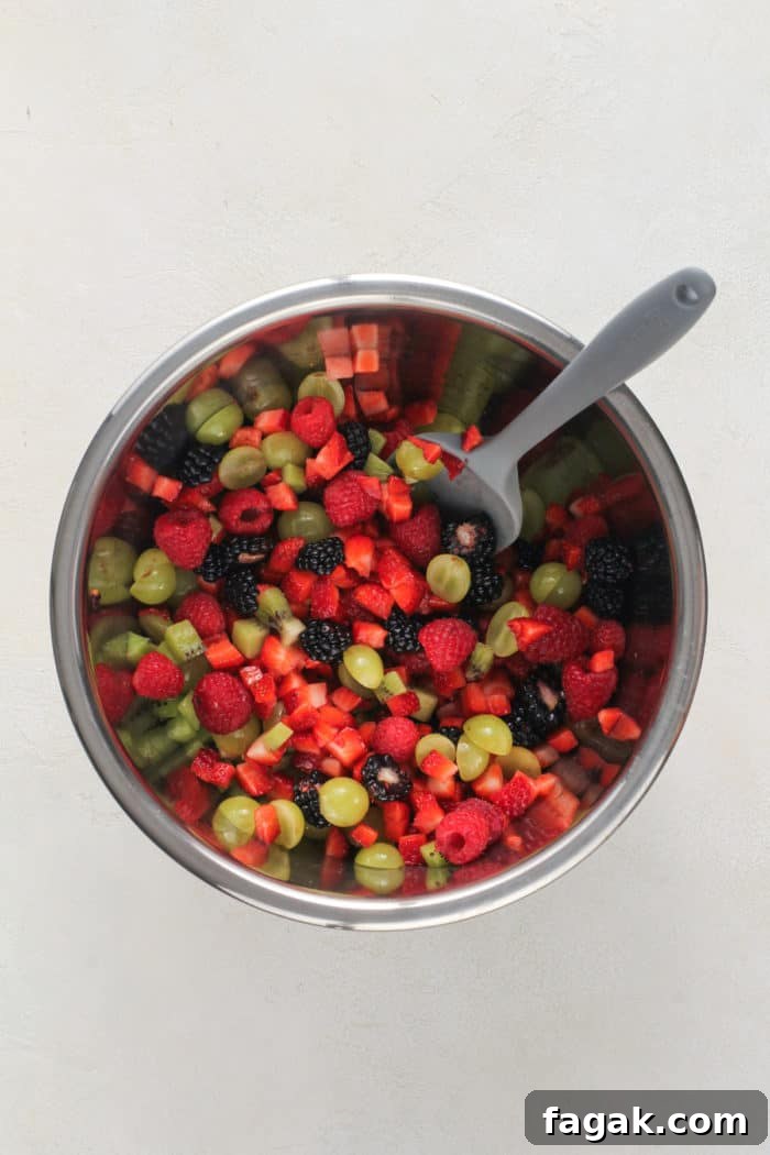 Spatula stirring diced fresh fruit in a metal bowl.