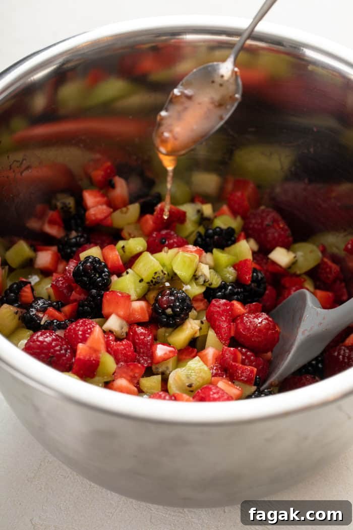 Spoon drizzling dressing over diced fresh fruit in a metal bowl.