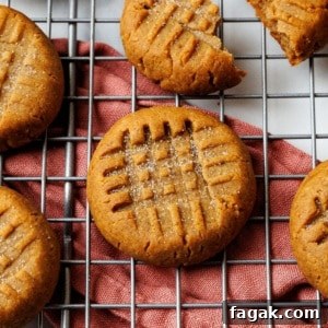 Single keto peanut butter cookie in focus on a wire rack over a rust napkin, with a deep criss-cross fork pattern.