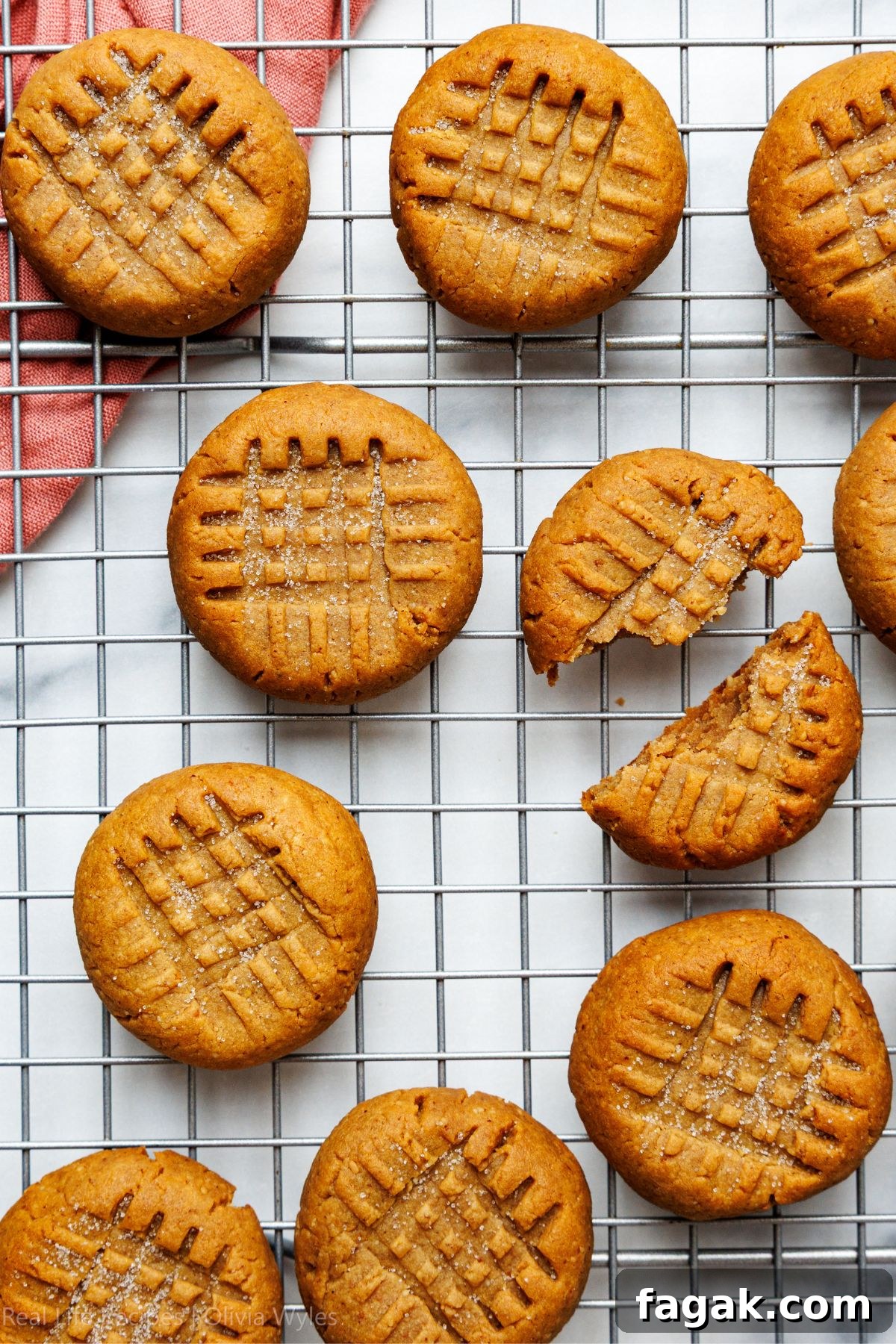 Overhead view of sugar-free peanut butter cookies on a wire rack, one broken in half showing the soft golden interior.