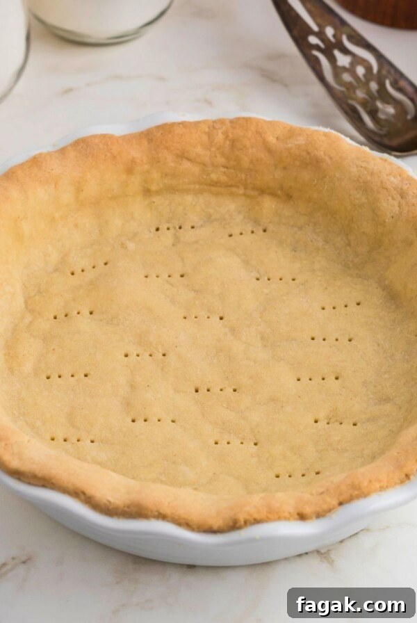 Golden brown baked pie crust in a white pie plate on a marble table.
