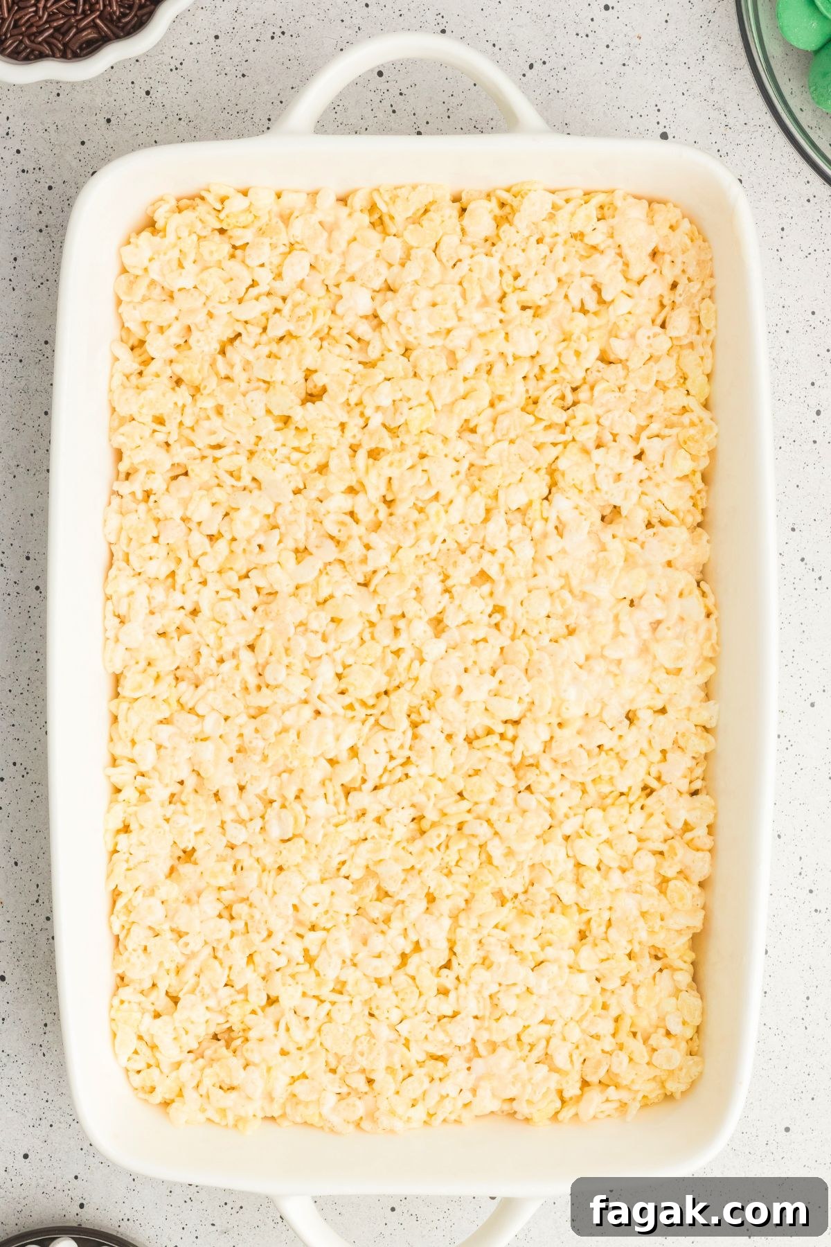 Rice krispie cereal mixed with melted marshmallows and butter in a white casserole dish.