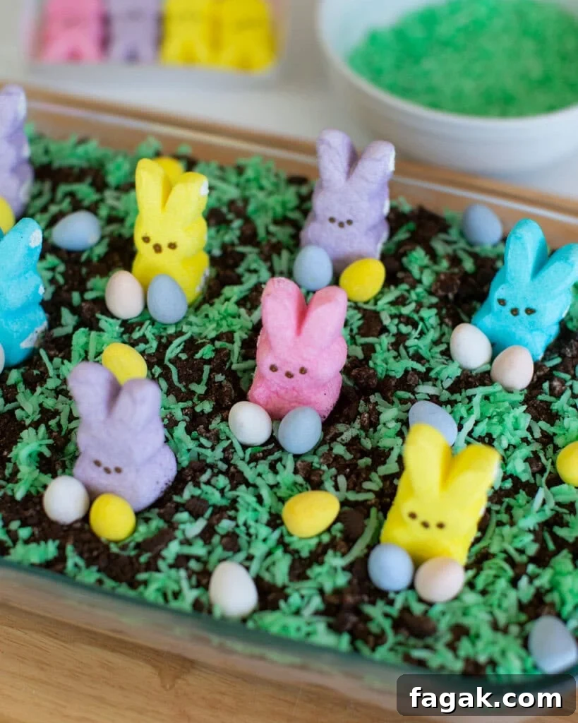 A festive dessert topped with green coconut grass, pastel-colored marshmallow bunnies, and small candy eggs. The bunnies are pink, purple, blue, and yellow, creating a colorful spring or Easter theme.