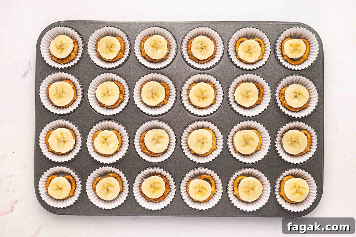Pretzels topped with a banana slice in a mini muffin pan with muffin liners.
