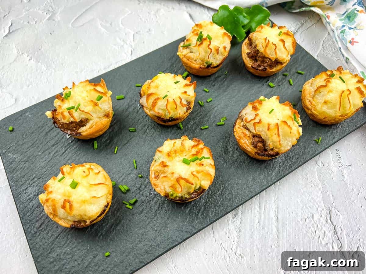 Eight Shepherd's Pie Bites are arranged on a slate board, garnished with chopped chives.