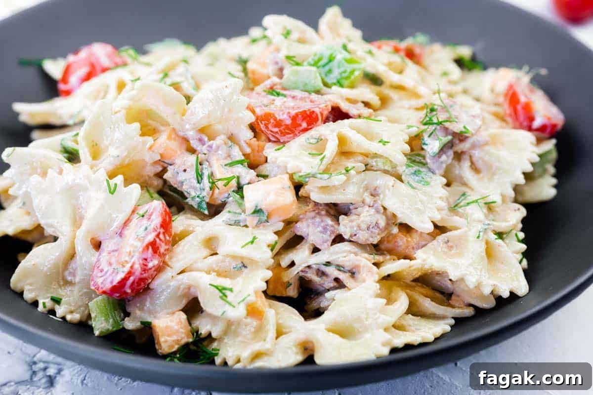 A black plate filled with creamy bowtie pasta, cherry tomatoes, diced vegetables, and herbs.