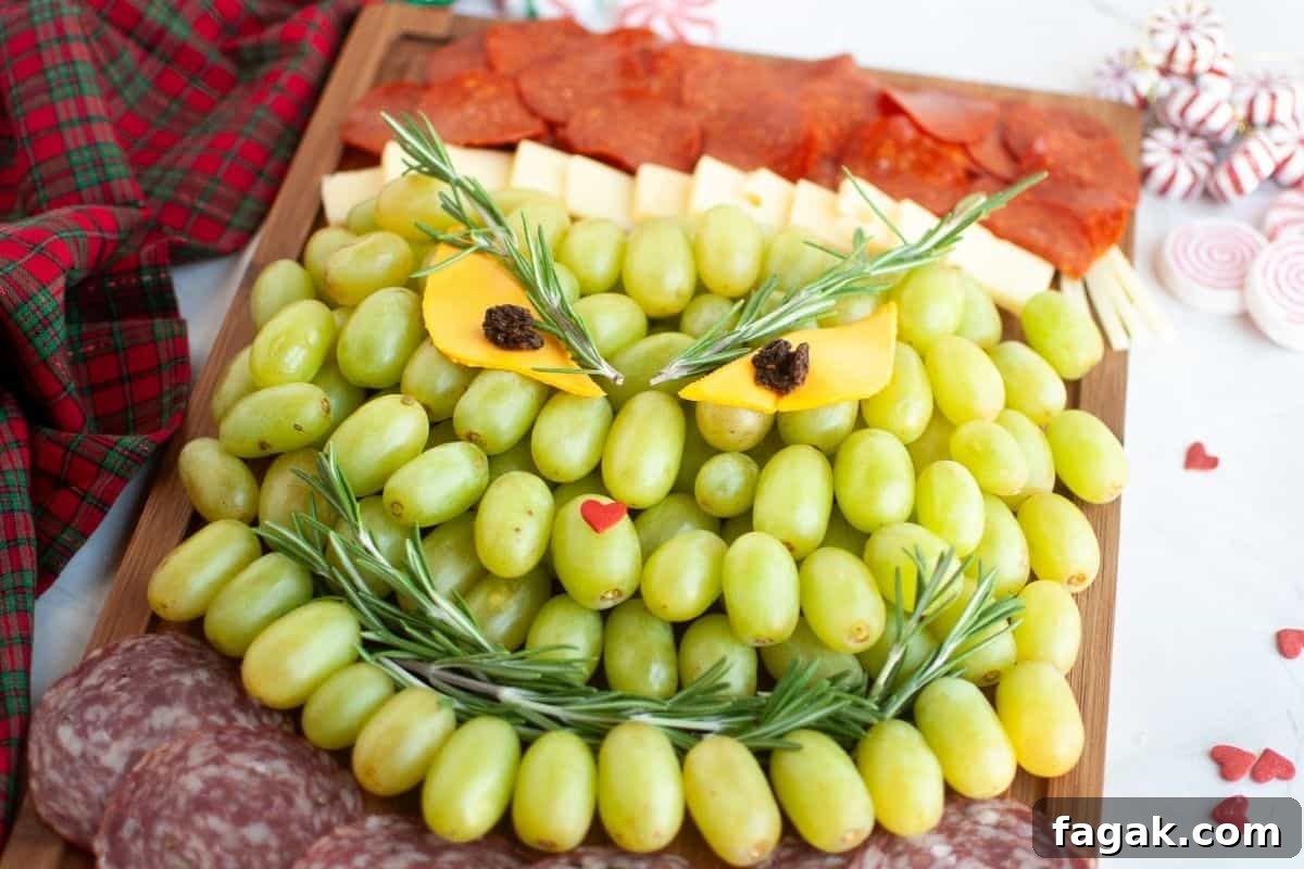 A charcuterie board arranged to resemble the Grinch's face, made with green grapes, cheese, meat slices, and garnished with rosemary.