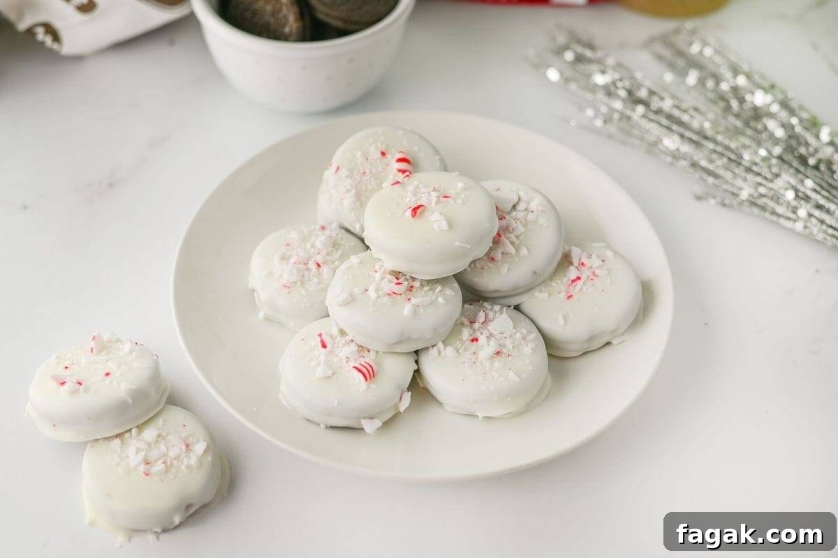 A white plate of Peppermint Crunch Oreos topped with crushed peppermint pieces sits on a white surface.