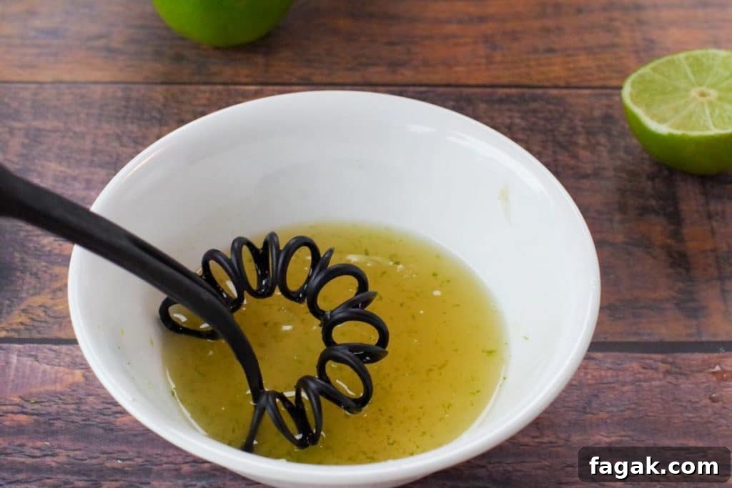 whisk mixing lime juice, honey and lime zest in white bowl