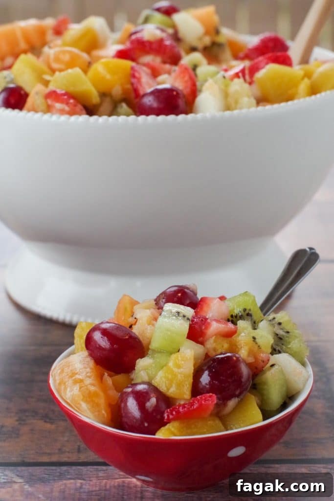 classic fruit salad in a small red bowl with white polkadots and a large white bowl of salad in the background