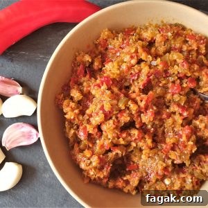 A bowl of jalapeno chili past with a red chili and cloves of garlic.