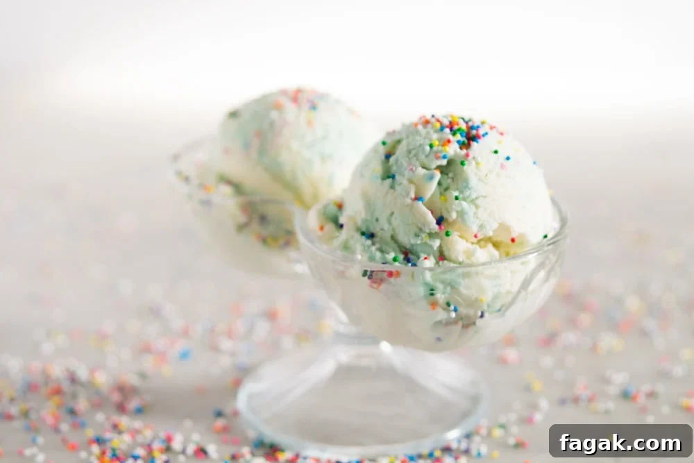 Two scoops of blue and white ice cream with colorful sprinkles in a glass container in front of a white background.
