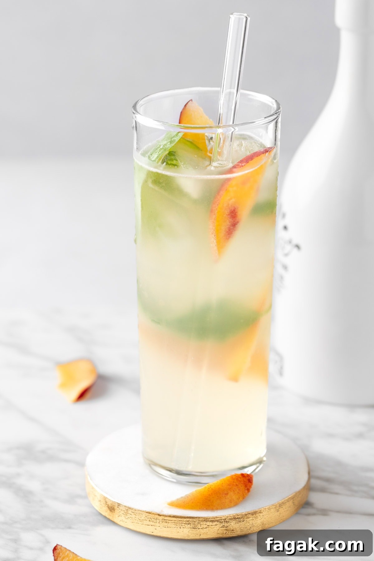 A peach basil mojito in a highball glass on a white background next to fresh peach slices.