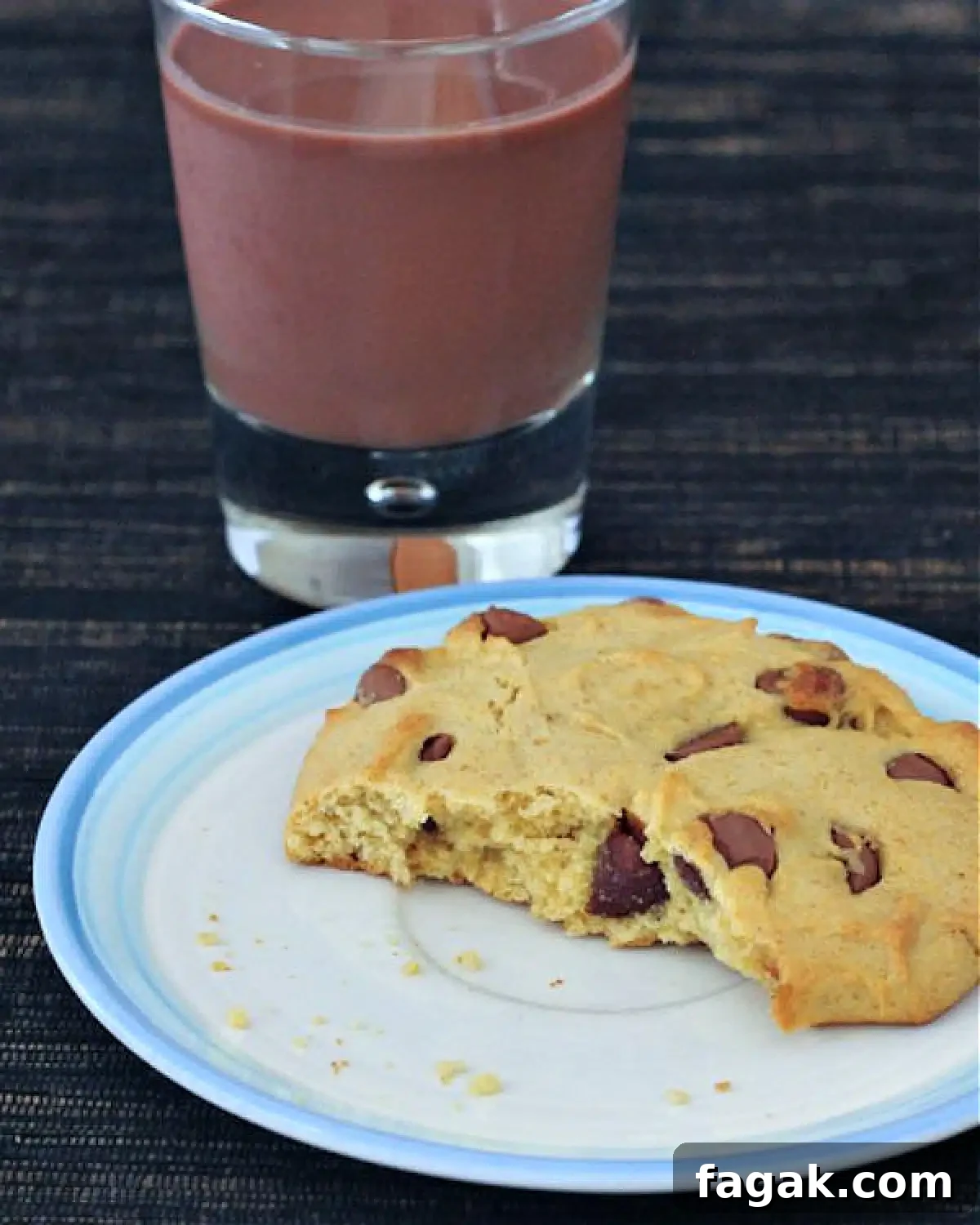 Single Serve Chocolate Chip Cookie @spabettie #glutenfree #vegan A single serve chocolate chip cookie with a bite out of it on a white plate. A short glass of chocolate milk sits next to the plate.