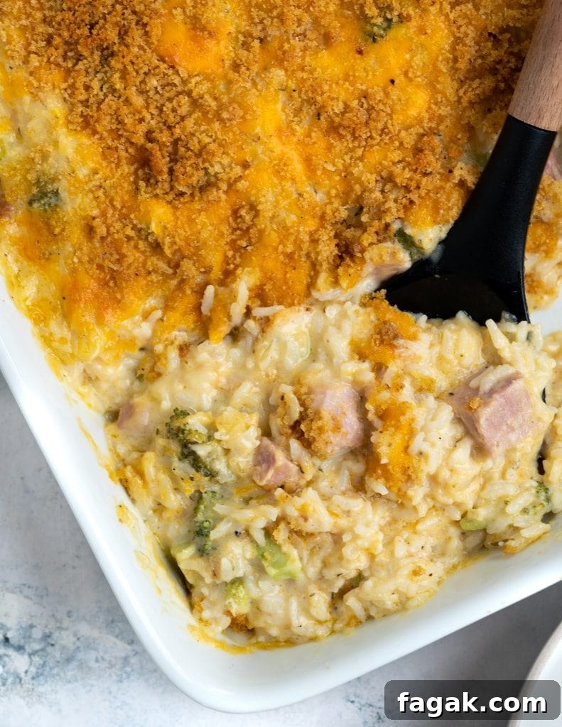 Corner of the casserole showing golden brown crust and underneath that a creamy mix of rice, ham, and broccoli.