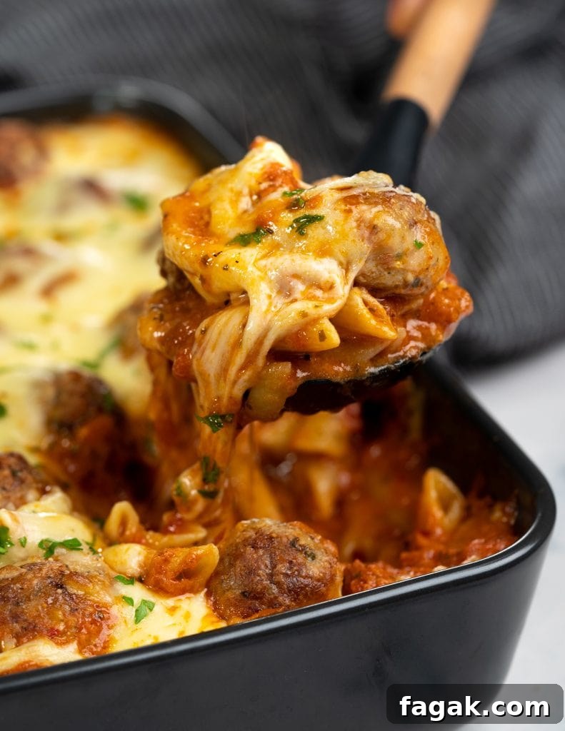 Slice of meatball casserole picked with a spatula showing strands of cheese and saucy pasta along with chunks of tender meatball