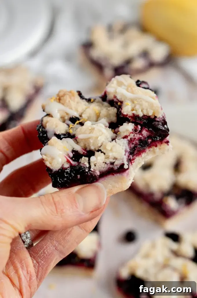 Lemon blueberry bars made with a buttery pale yellow shortbread base with purply blue blueberry filling and a shortbread crumble on top.