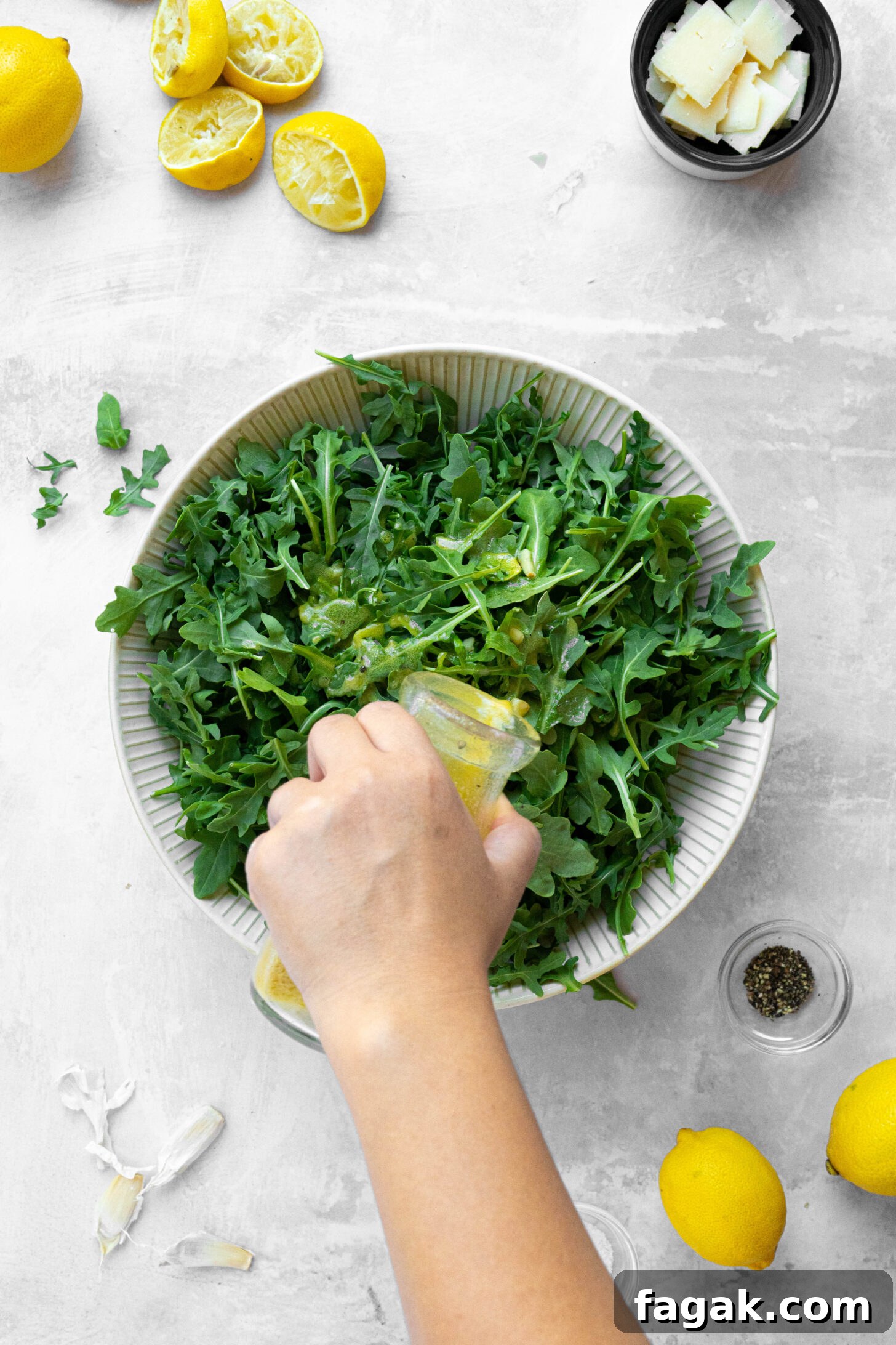 Citrus Arugula Salad with Lemon Vinaigrette 3 A hand pouring lemon dressing over a bowl of arugula.