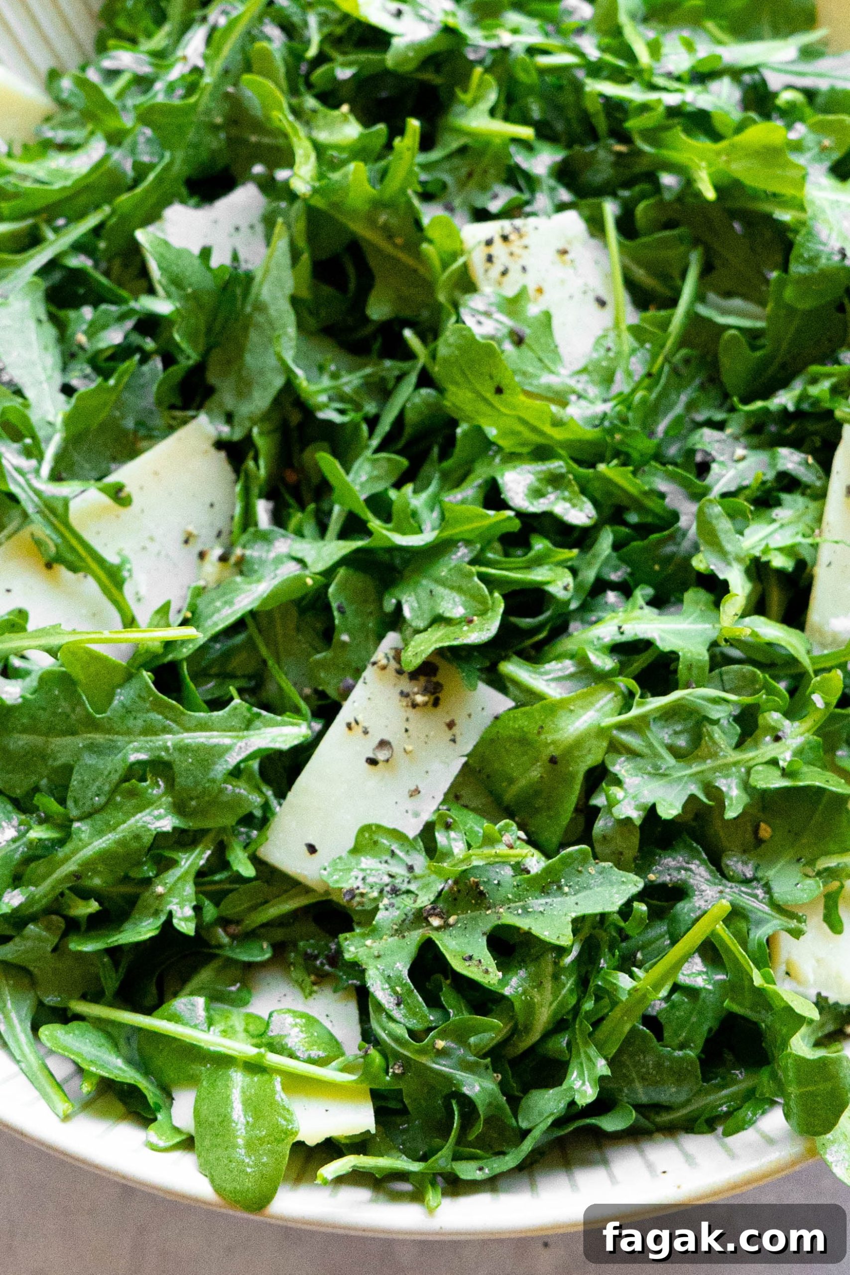 Citrus Arugula Salad with Lemon Vinaigrette 5 A white bowl with arugula and shaved parmesan.