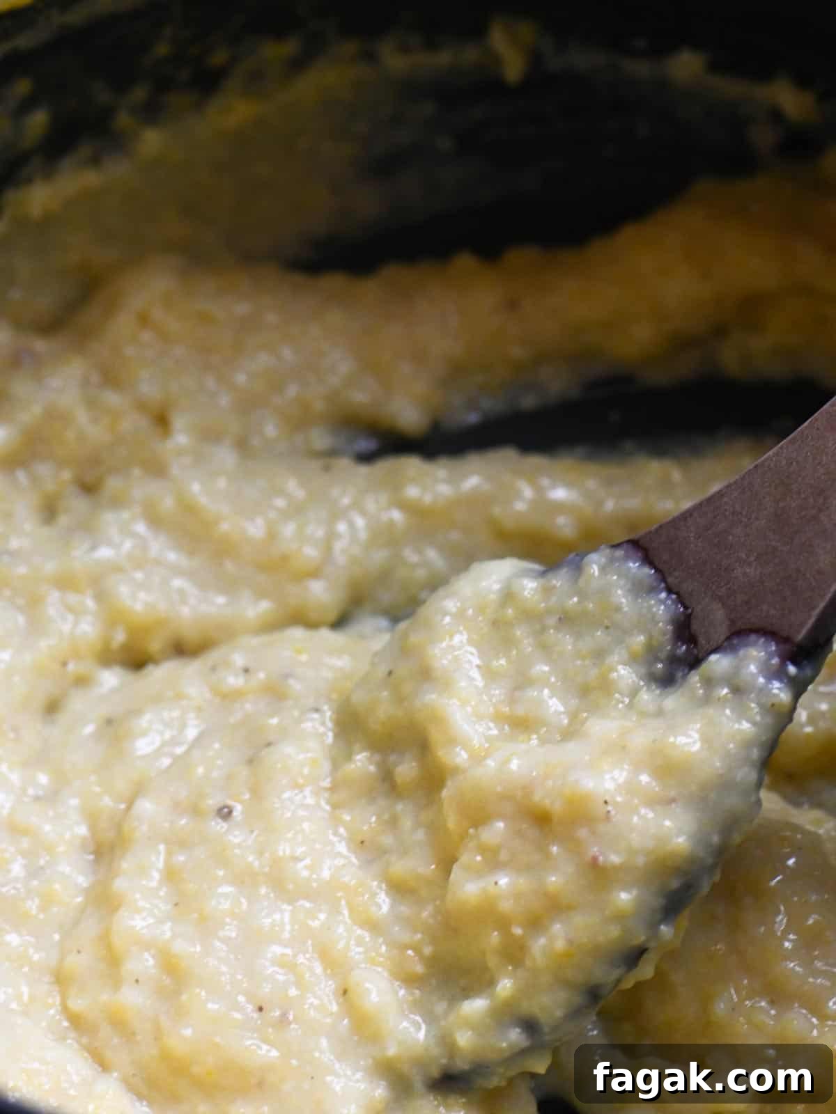 Creamy polenta being stirred with a wooden spoon in a pot.