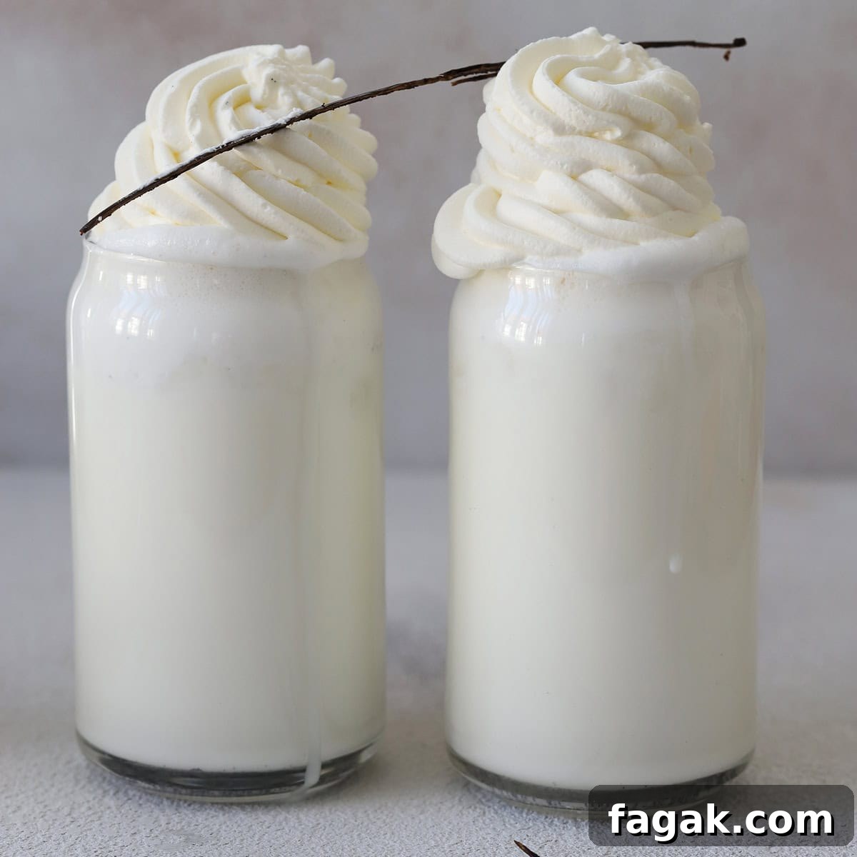 Two glasses of Starbucks vanilla bean frappuccino with whipped cream and a vanilla bean pod garnish.