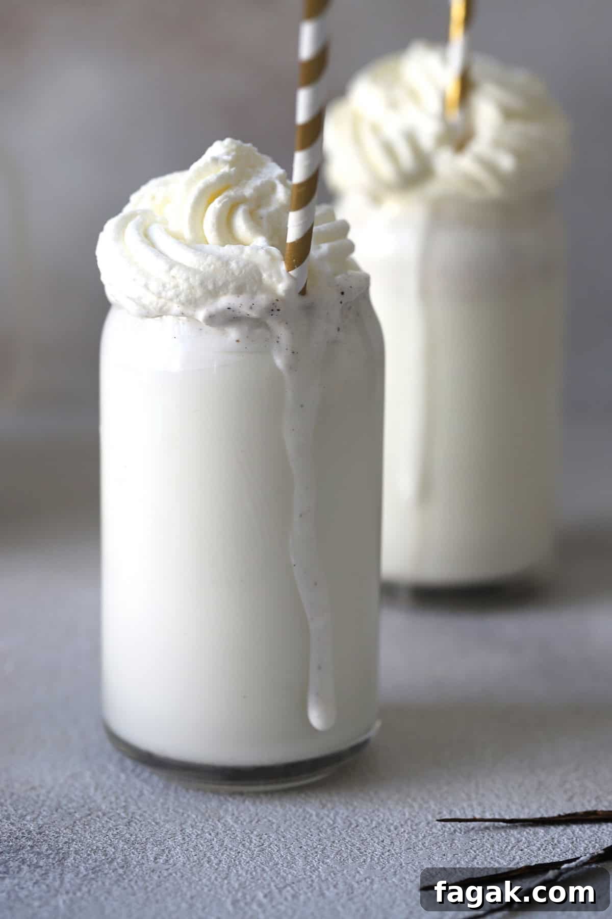Two glasses of Starbucks vanilla bean frappuccino topped with whipped cream and straws.
