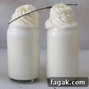 Two glasses of Starbucks vanilla bean frappuccino with whipped cream and a vanilla bean pod garnish.