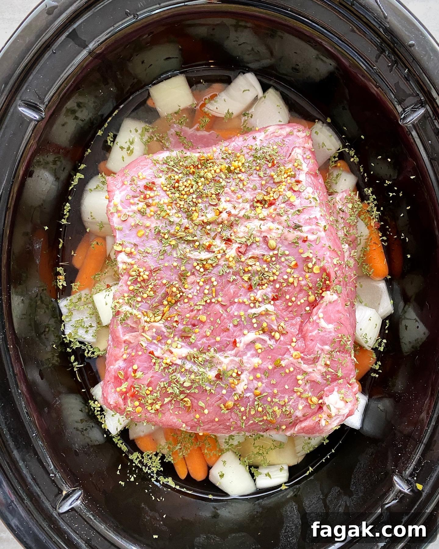 overhead shot of uncooked corned beef with potatoes, carrots, and onion in a black slow cooker