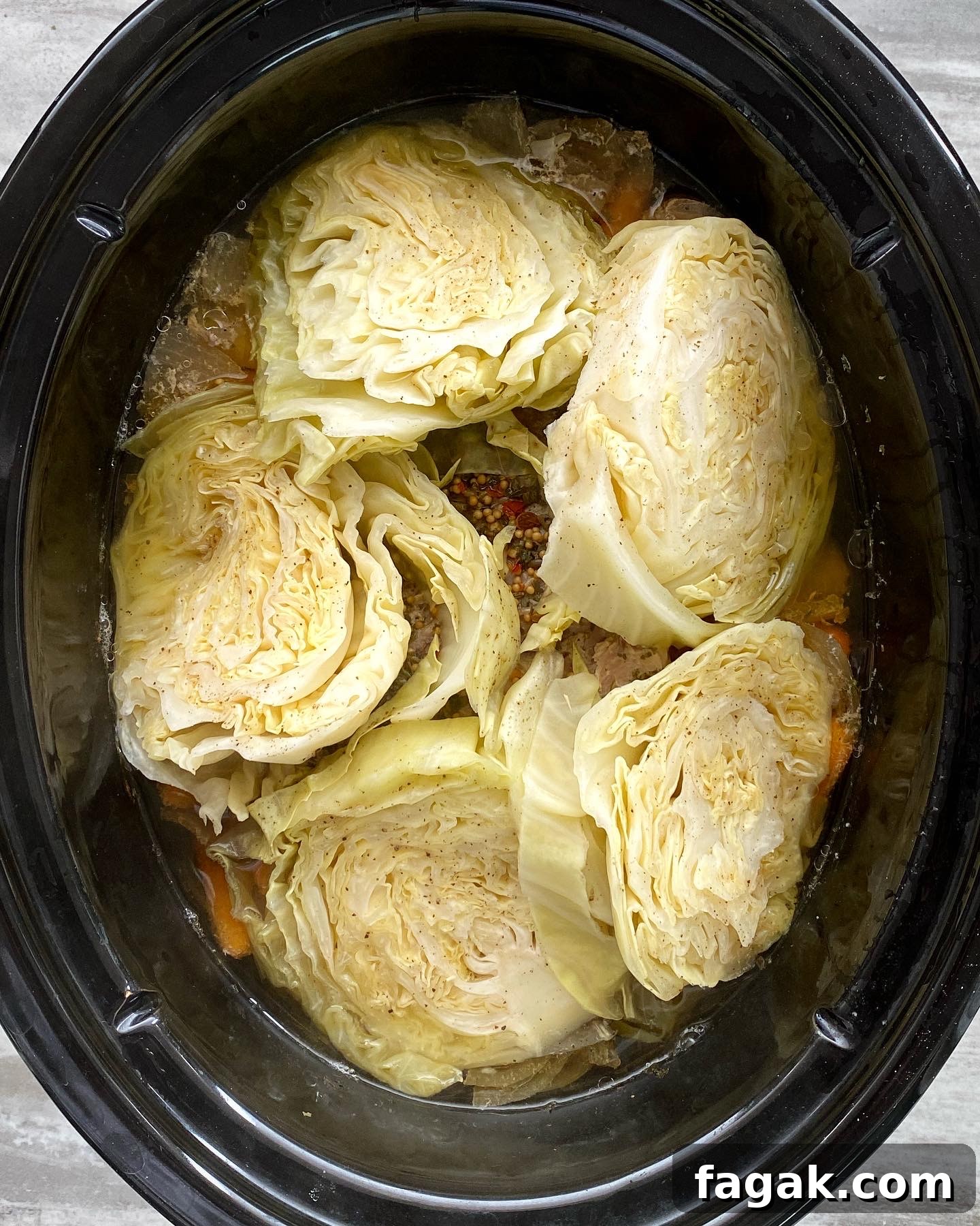 overhead shot of cooked corned beef with potatoes, carrots, and onion in a black slow cooker with cooked cabbage wedges on top