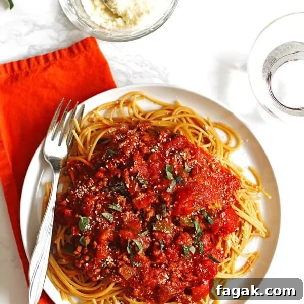 Spaghetti sauce and noodles on a white plate with fresh herbs garnishing it.