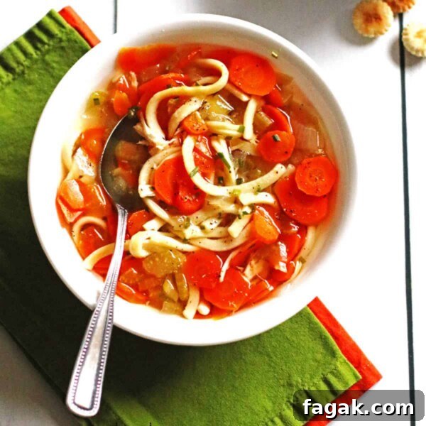 A bowl of chicken soup in a white bowl with a spoon in it