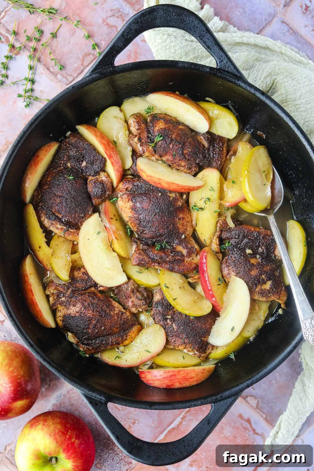 Apple cider chicken in a cast-iron skillet with a silver spoon.