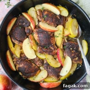 Apple cider chicken in a cast-iron skillet with a silver spoon.