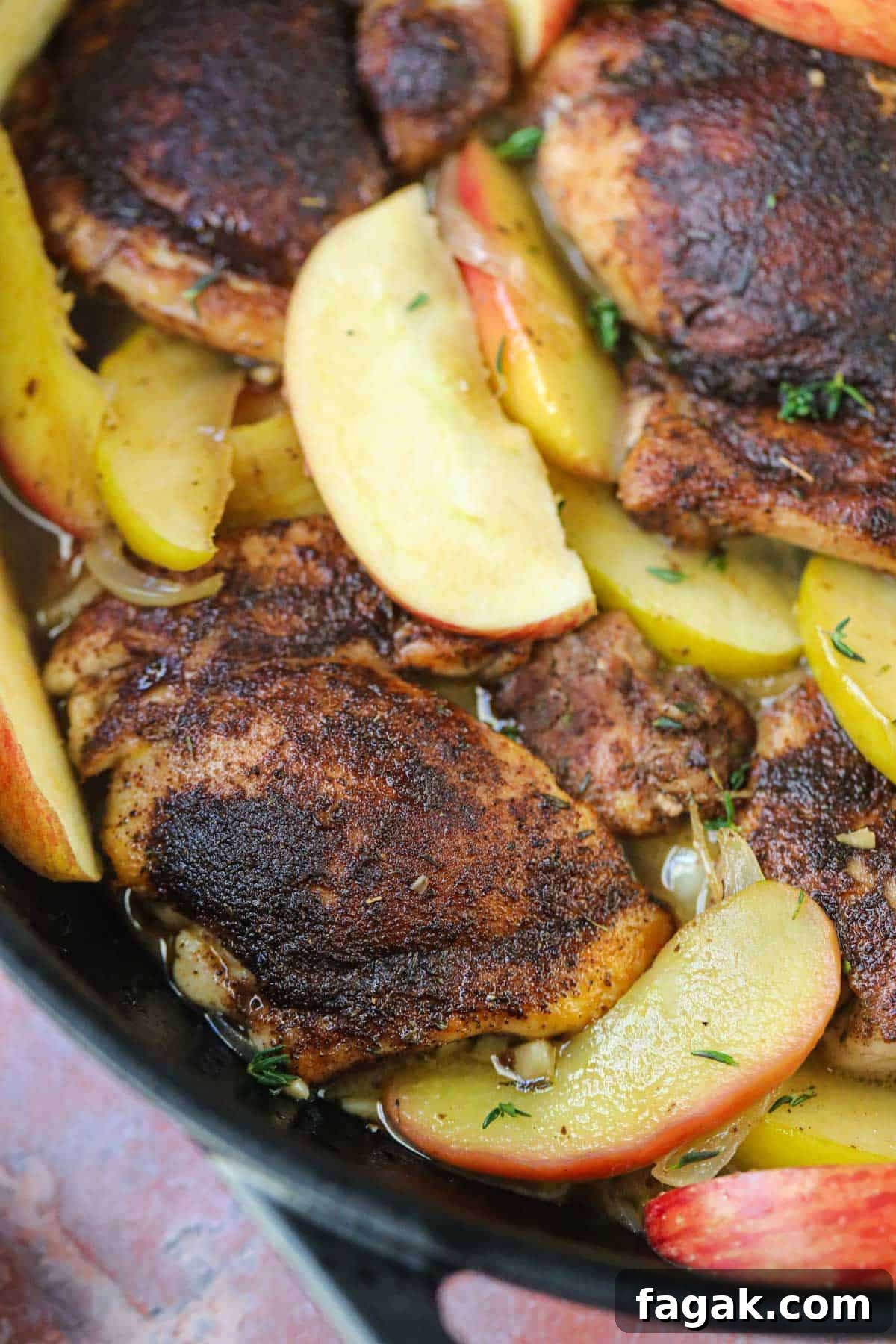 Apple cider chicken in a cast-iron skillet with a silver spoon.