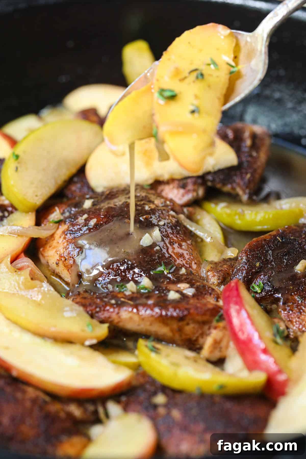 sauce being spooned over apple cider chicken in a skillet.