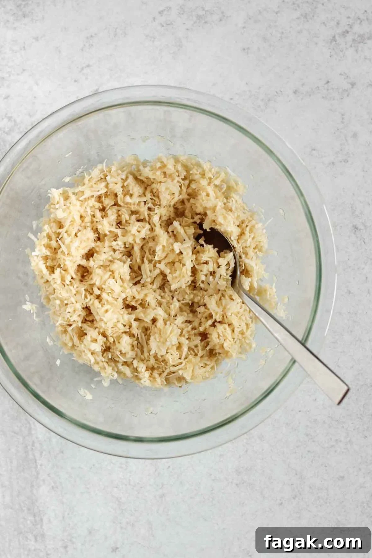 Shredded coconut mixed with egg whites and maple syrup in a medium glass mixing bowl.