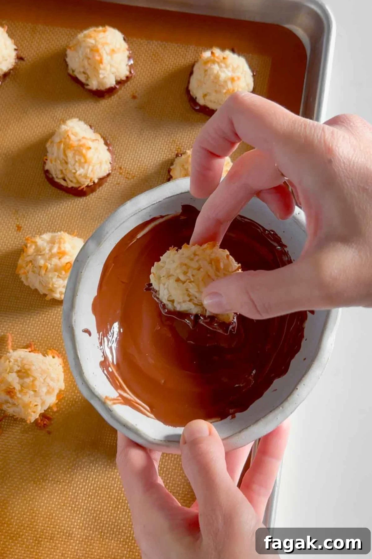 Hand dipping a single coconut macaroon cookie into a bowl of melted chocolate.