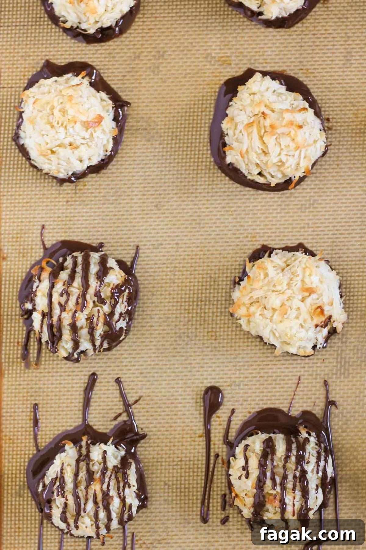 Coconut macaroon cookies that have been dipped in chocolate, some also drizzled with chocolate, on a baking sheet.