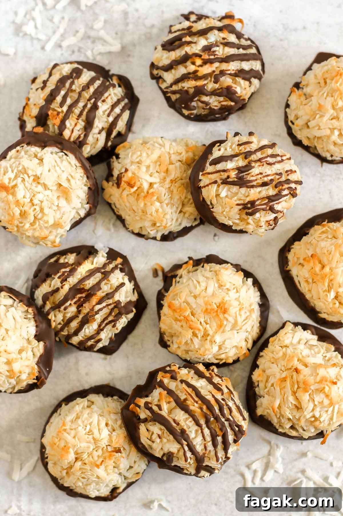 Coconut macaroons dipped in chocolate and some of them drizzled with chocolate laid out on a gray surface with shredded coconut sprinkled about.