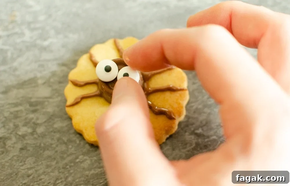 Adding eyes to spider body Cute Spider Halloween Biscuits on marble worktop