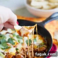 Hand with a tortilla chip dipping into Mushroom and Chorizo Queso Dip.