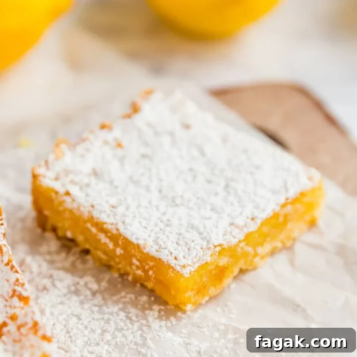 A lemon square on a piece of parchment with a cut lemon behind it.