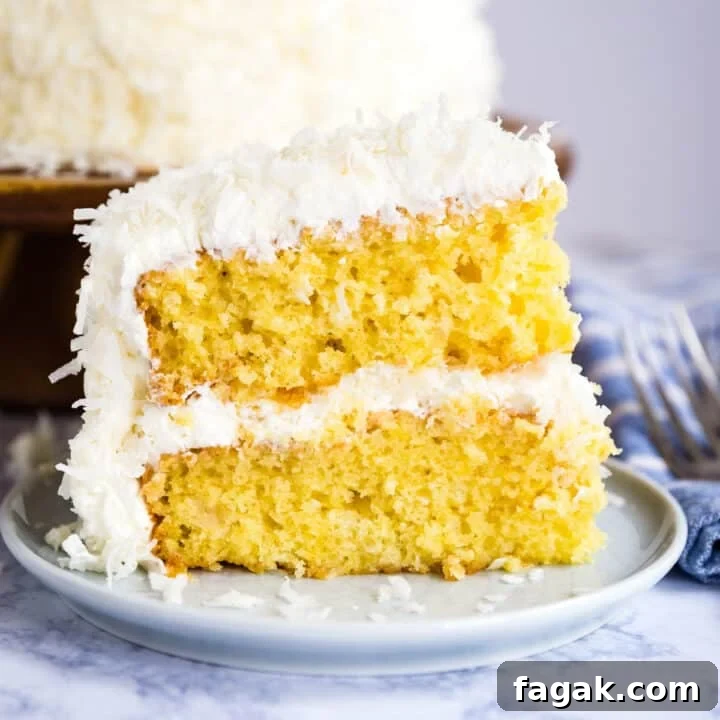 A slice of coconut cake on a plate with the full cake behind it.