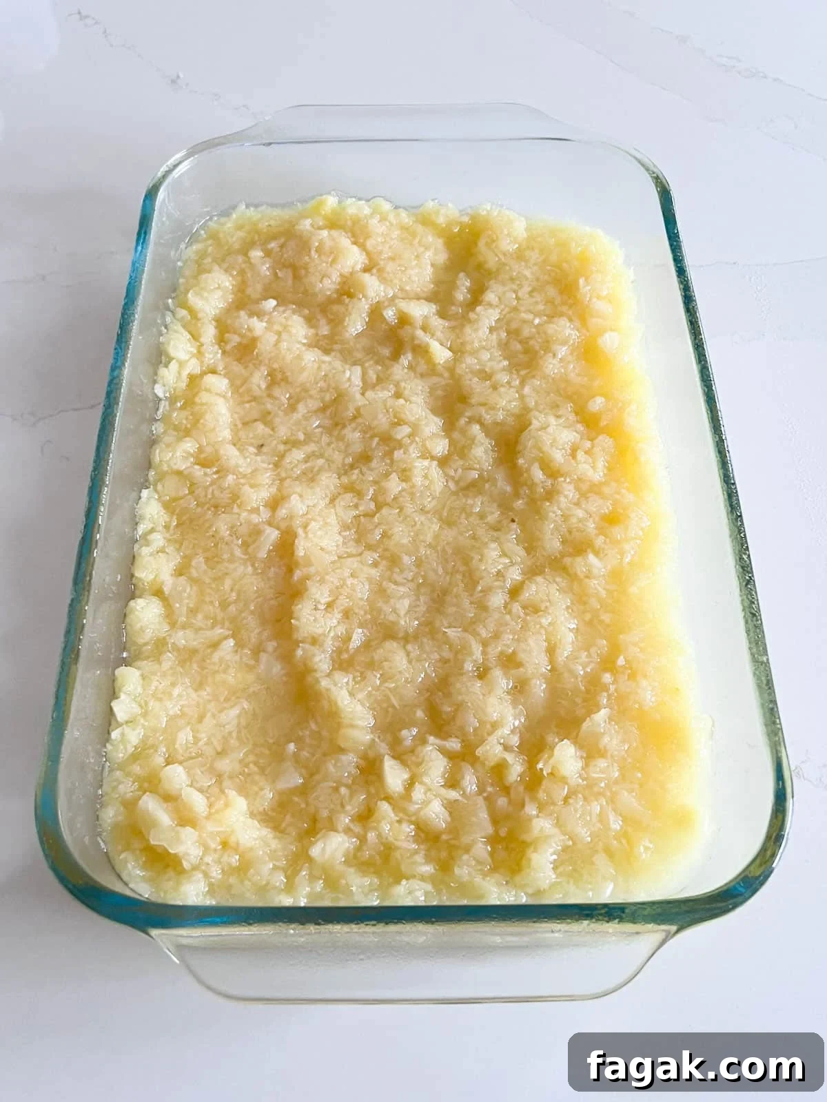 A clear glass baking pan with crushed pineapple spread along the bottom of it.