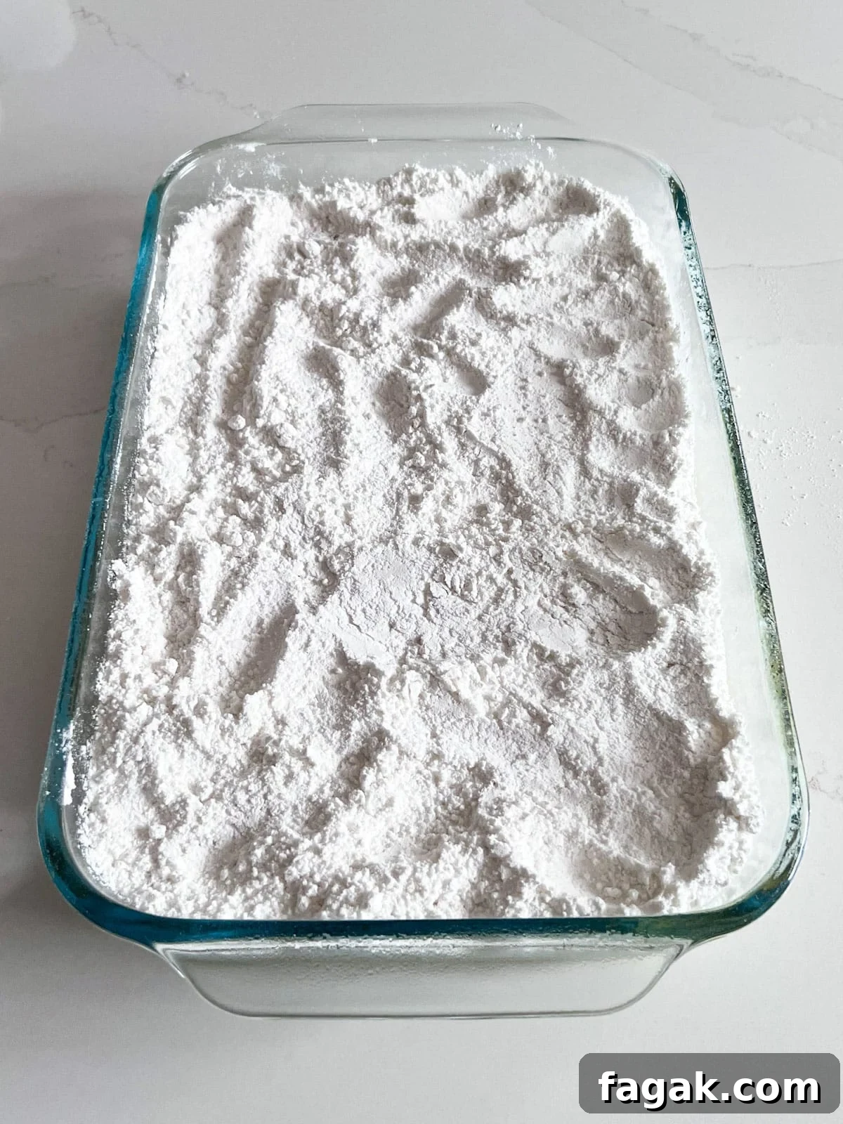 A layer of cake mix added on top of the pineapple layer in a glass baking pan.