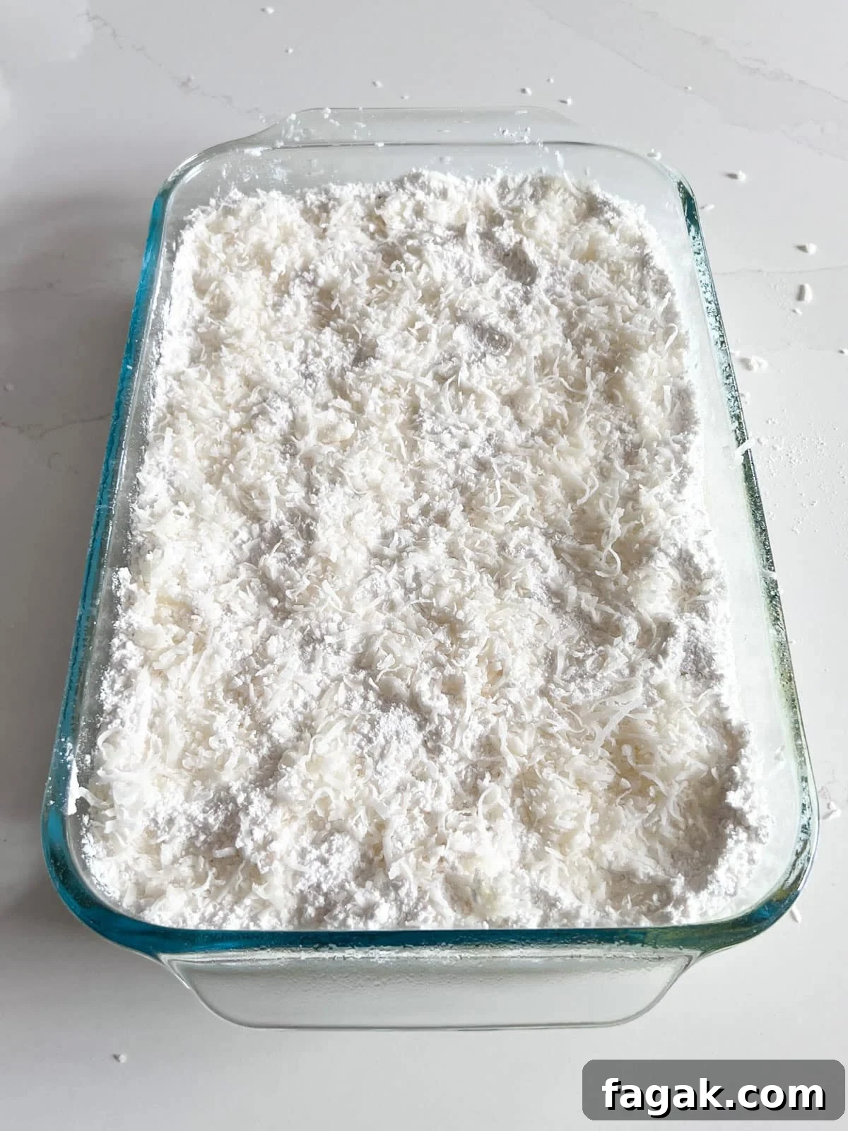 A layer of coconut sprinkled on top of the cake mix layer in a glass baking pan.